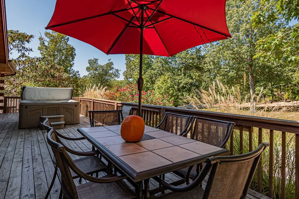 This image features a cheerful outdoor dining area with a red umbrella, a dining table set for a group, a festive pumpkin centerpiece, and lush greenery surrounding the scene. The setting is lively and inviting, ideal for gatherings and celebrations.
