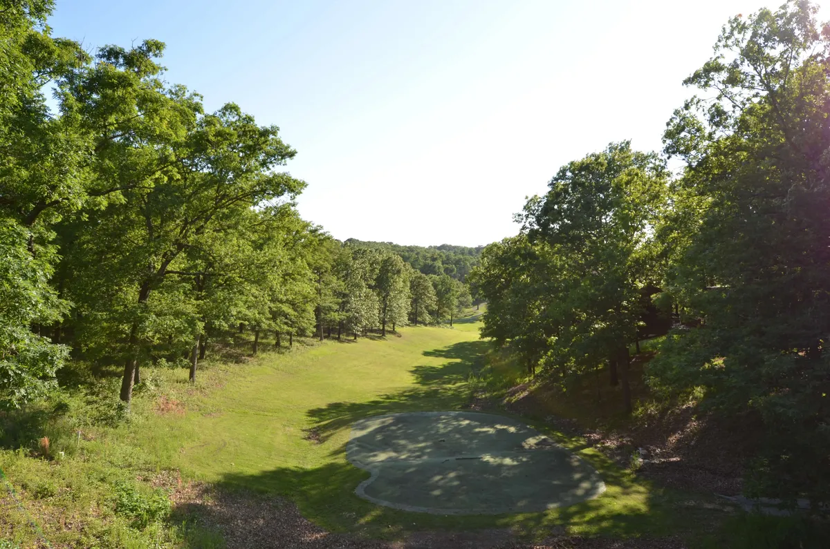 A peaceful view of an open grassy area bordered by a tree line, featuring a well-manicured golf putting green in the foreground under a wide sky. The natural setting hints at sunset lighting, with the possibility of seeing wildlife or stargazing at night.