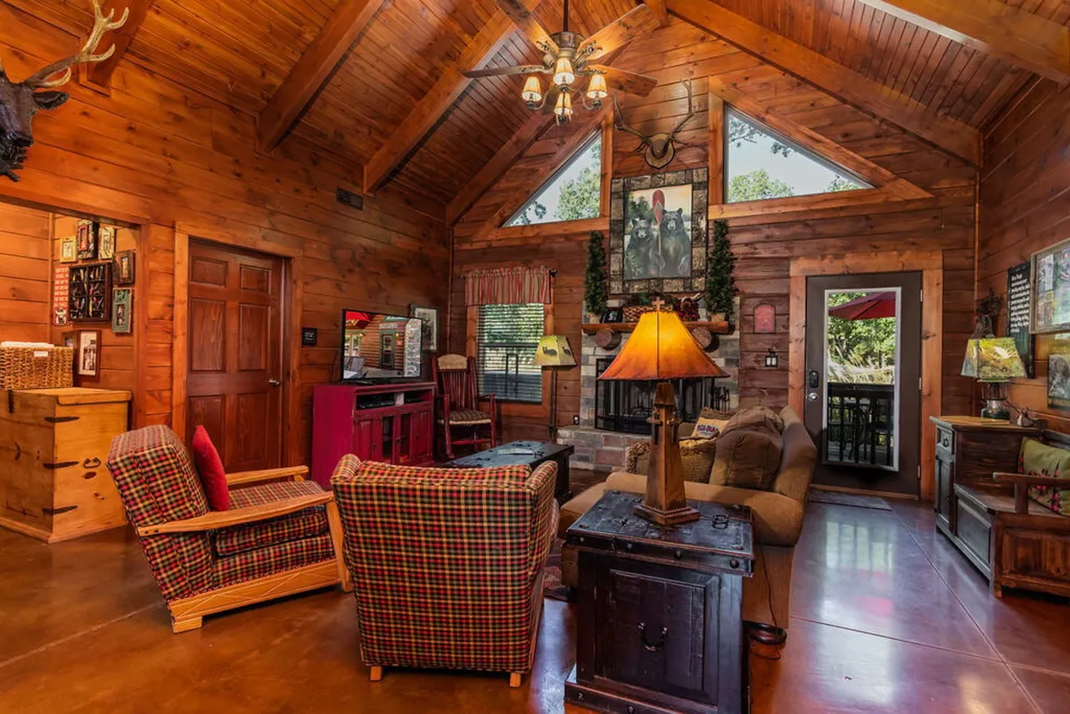 This image features a soaring wooden ceiling, a dramatic stone fireplace, and cozy checkerboard chairs arranged for gatherings. The space is filled with warm lighting and decorative wall art, creating an inviting and communal atmosphere.