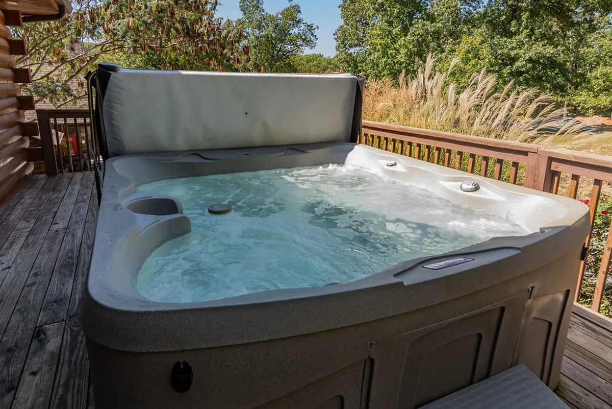 A private hot tub set on a wooden deck, surrounded by lush greenery. The tranquil scene suggests relaxation and immersion in nature, with the hot tub positioned to offer soothing woodland views.