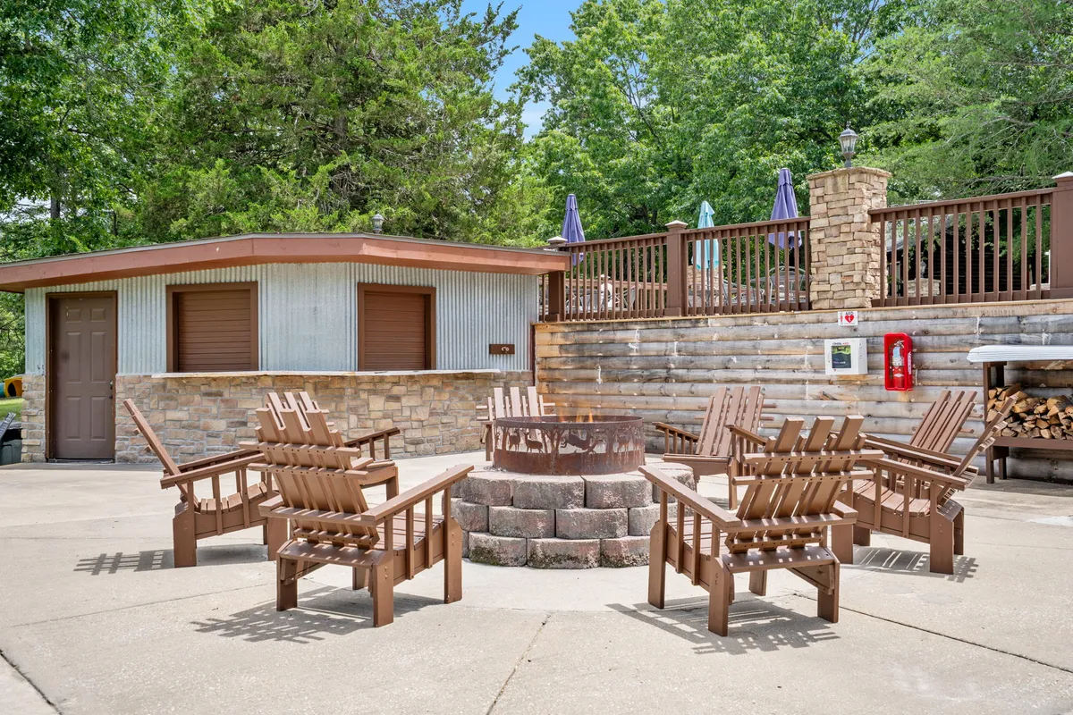A welcoming exterior scene with a fire pit surrounded by Adirondack chairs on a stone patio next to a charming wooden cabin. The setup suggests a relaxed atmosphere for evening socializing and making s'mores under the stars.
