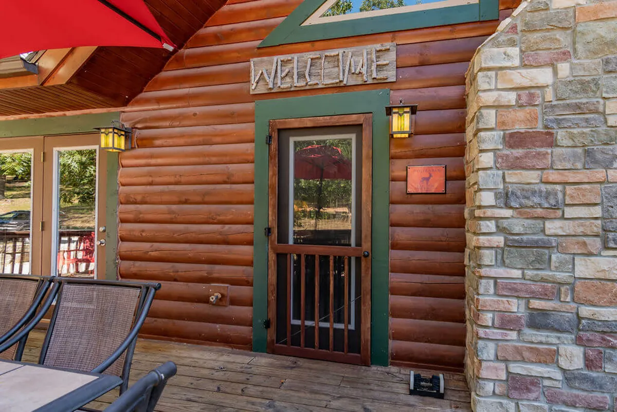 An inviting exterior with a wooden welcome sign, front door, stone wall, and a comfortable outdoor seating area. The deck area is perfect for casual gatherings and provides a glimpse of the welcoming atmosphere awaiting guests.