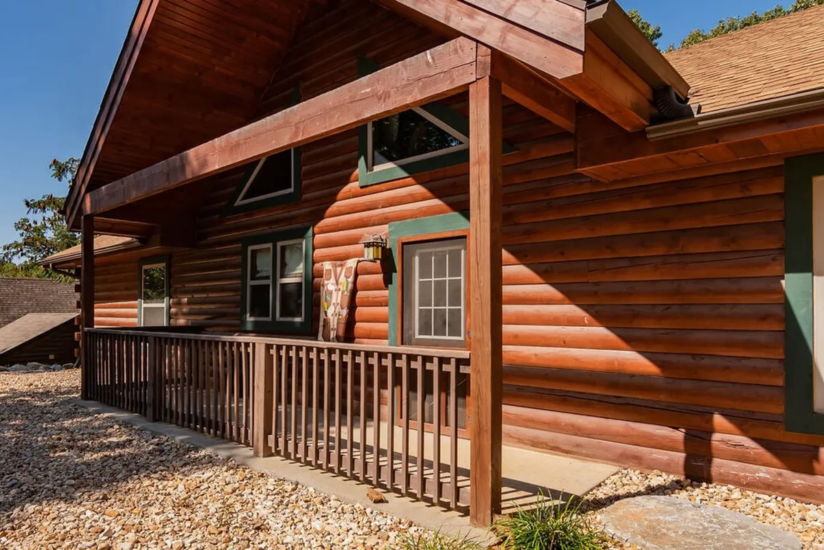 A charming log-cabin porch with wooden railing and green accents invites guests to relax while overlooking surrounding greenery. The porch is designed for comfort and includes seating perfect for coffee or casual conversation.
